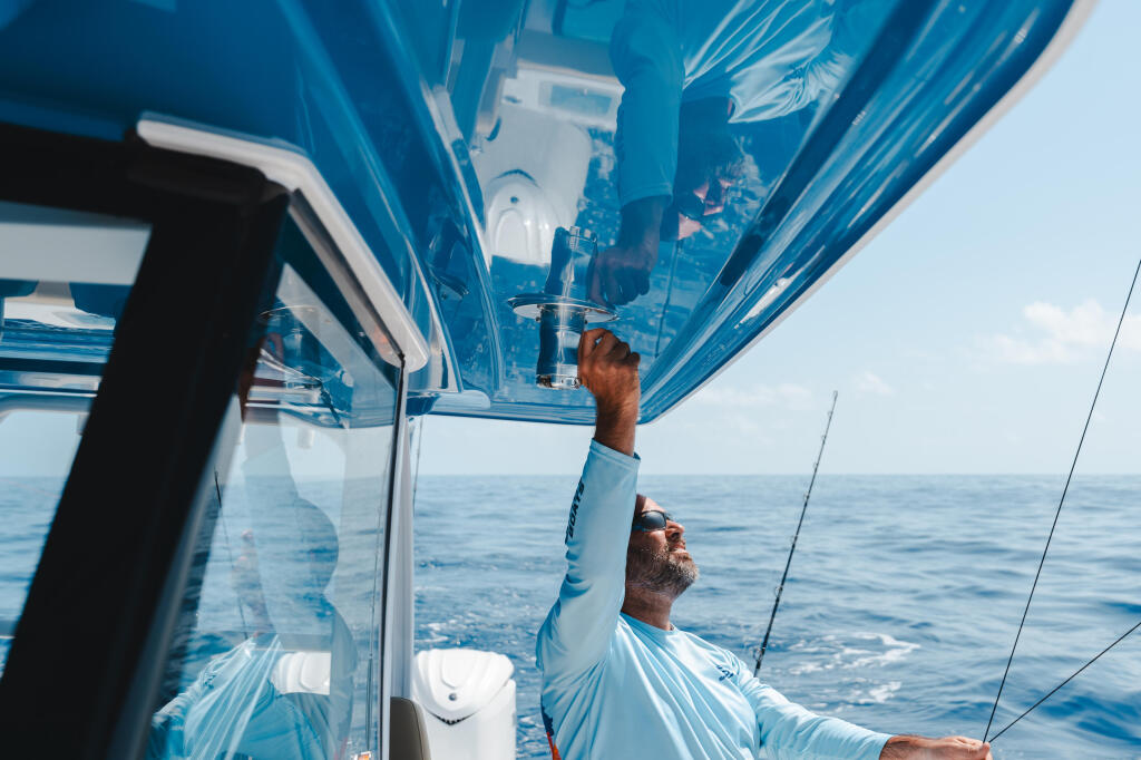 Angler reaching up to adjust the hard-top while fishing offshore with rods visible in the background