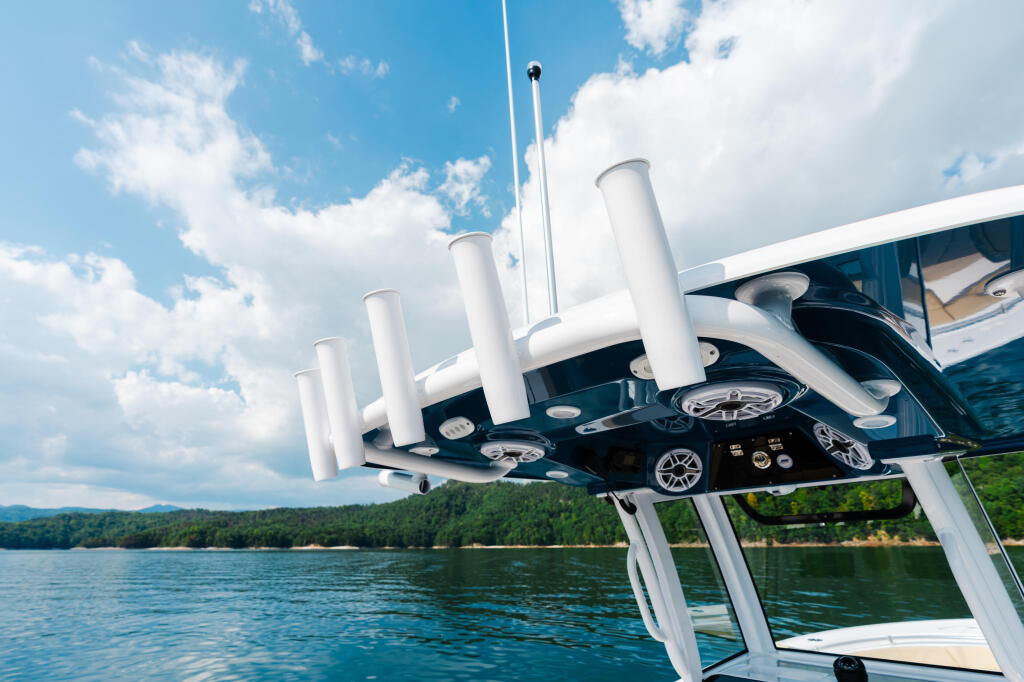 Overhead view of boat helm with twin engines, white hardtop, and antenna on calm lake with forested shoreline