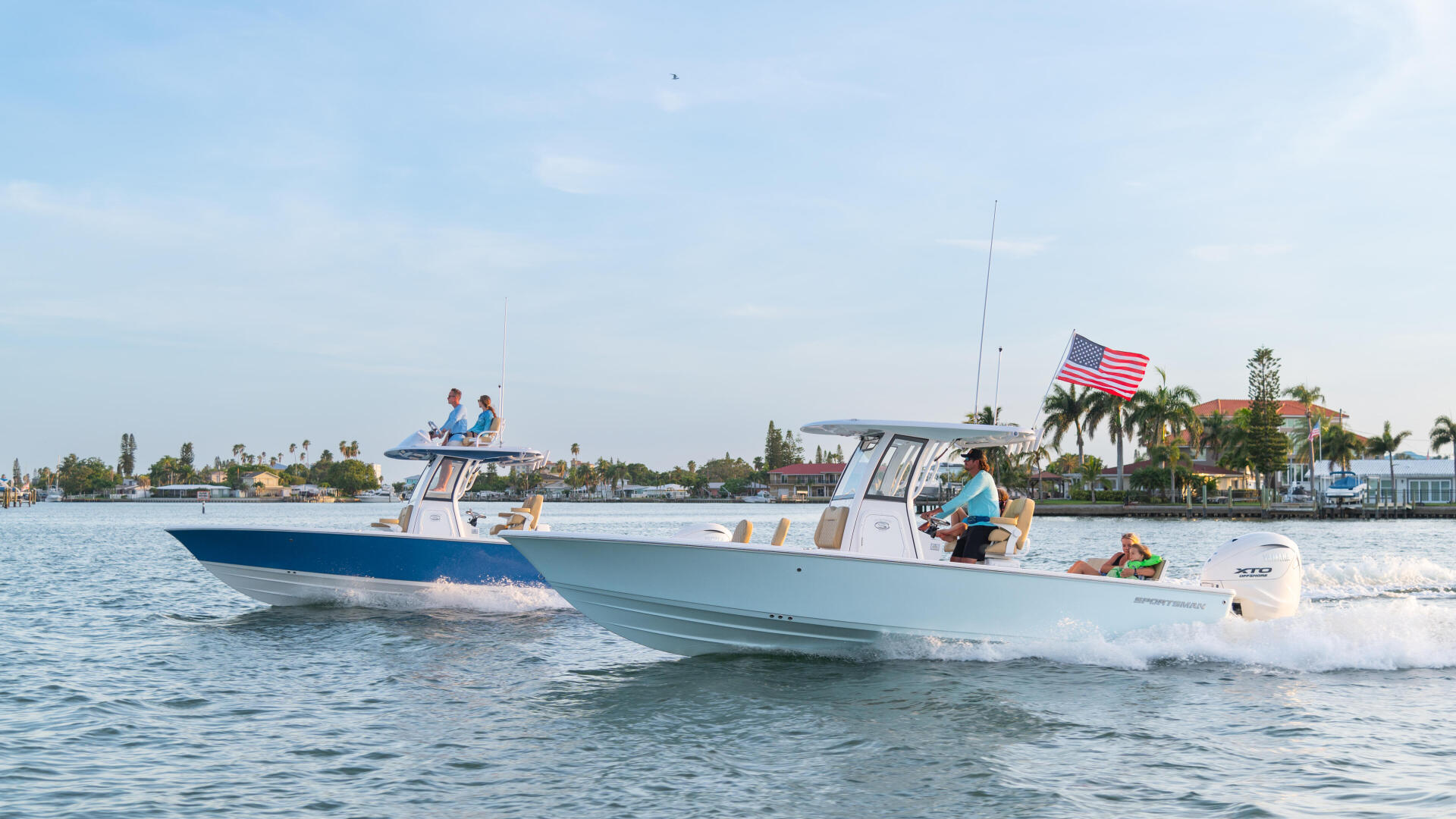 Two center console boats anchored in shallow water near a sandy beach with families and children aboard