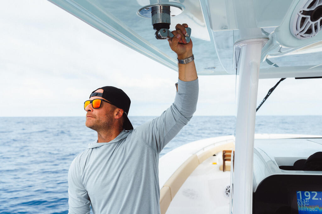Angler in sunglasses adjusts rigging on hardtop of offshore fishing boat
