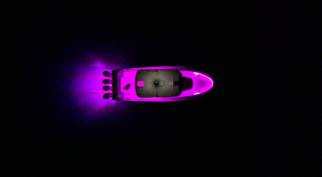 Bright magenta recreational boat with RGB lighting illuminating the hull against a dark background