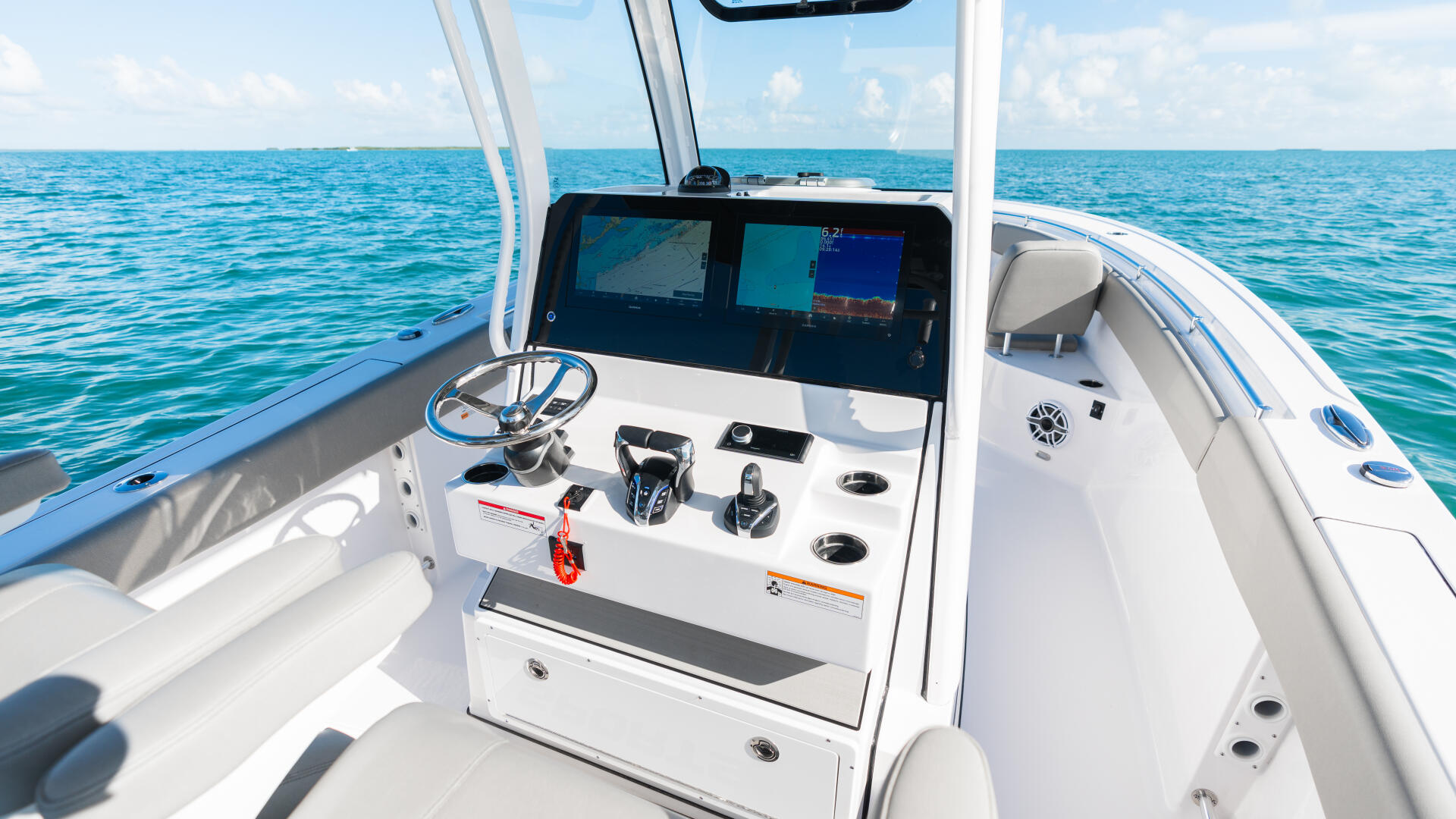 Helm station of center console boat with dual monitors, steering wheel, and electronic controls overlooking calm blue water