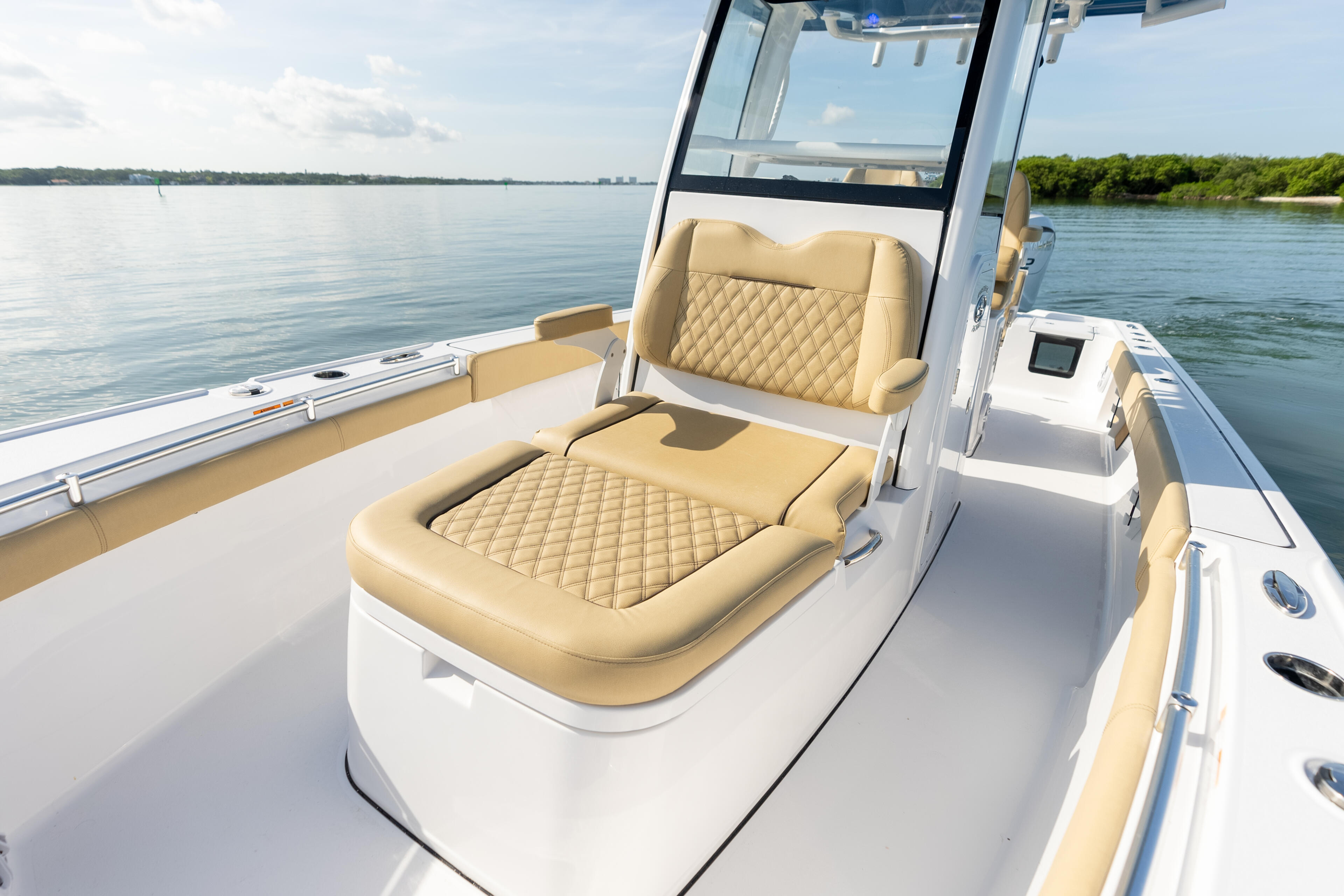 Cream-colored quilted seating and helm console on a white center console boat with calm water and green shoreline behind