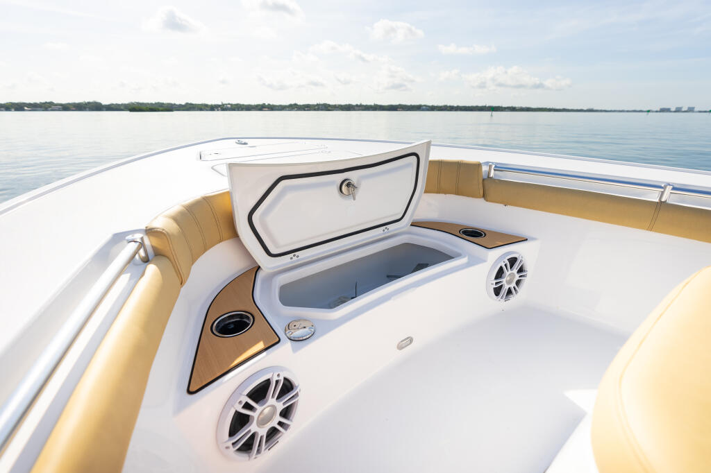 Open storage box on boat deck with tan cushioned seating and calm water backdrop