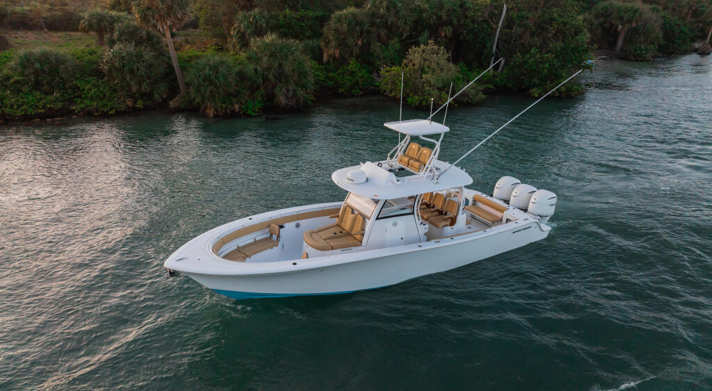 White sport fishing boat with tan seating and dual outboard engines anchored in clear turquoise water near mangrove shoreline