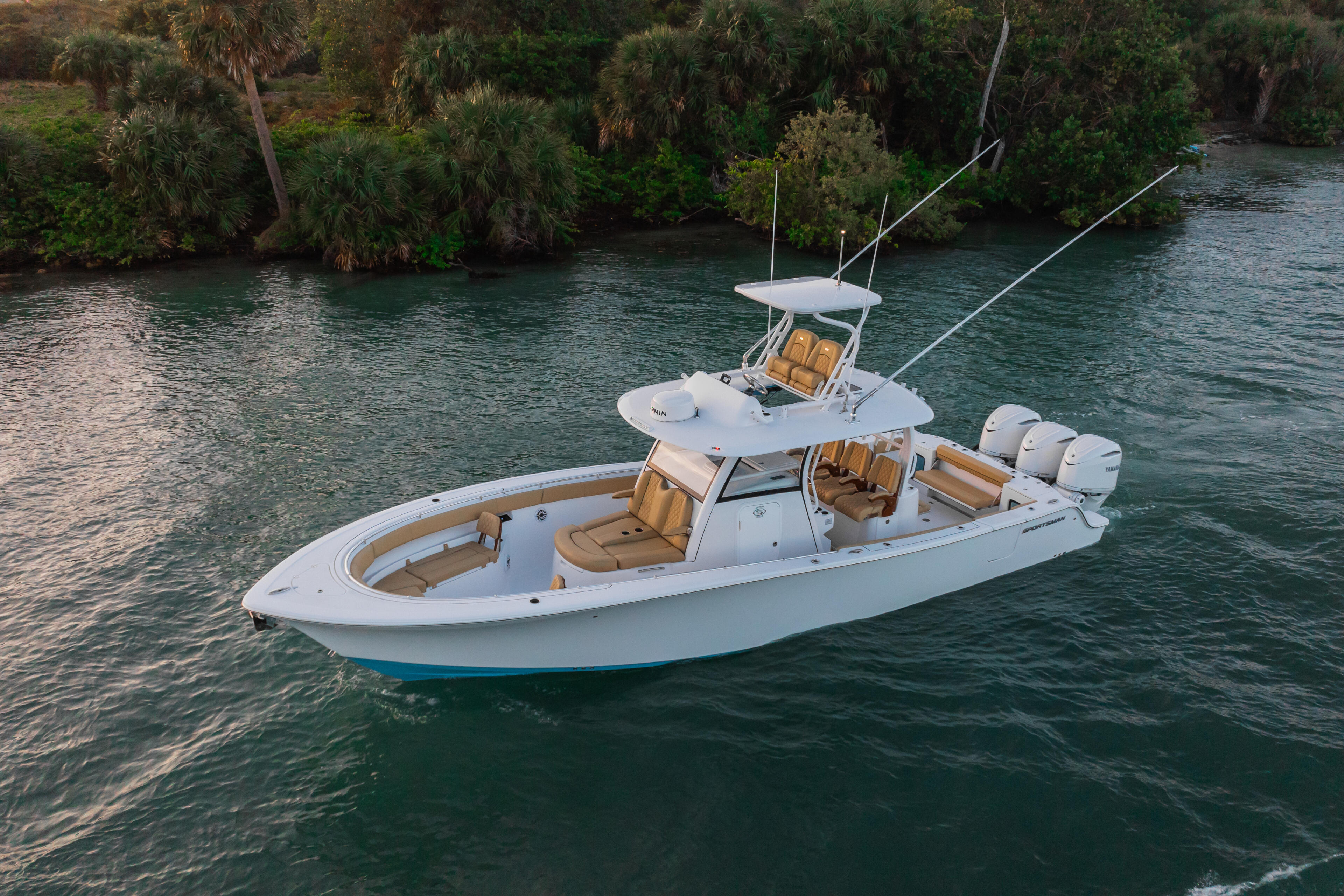 White sport fishing boat with tan seating and dual outboard engines anchored in clear turquoise water near mangrove shoreline