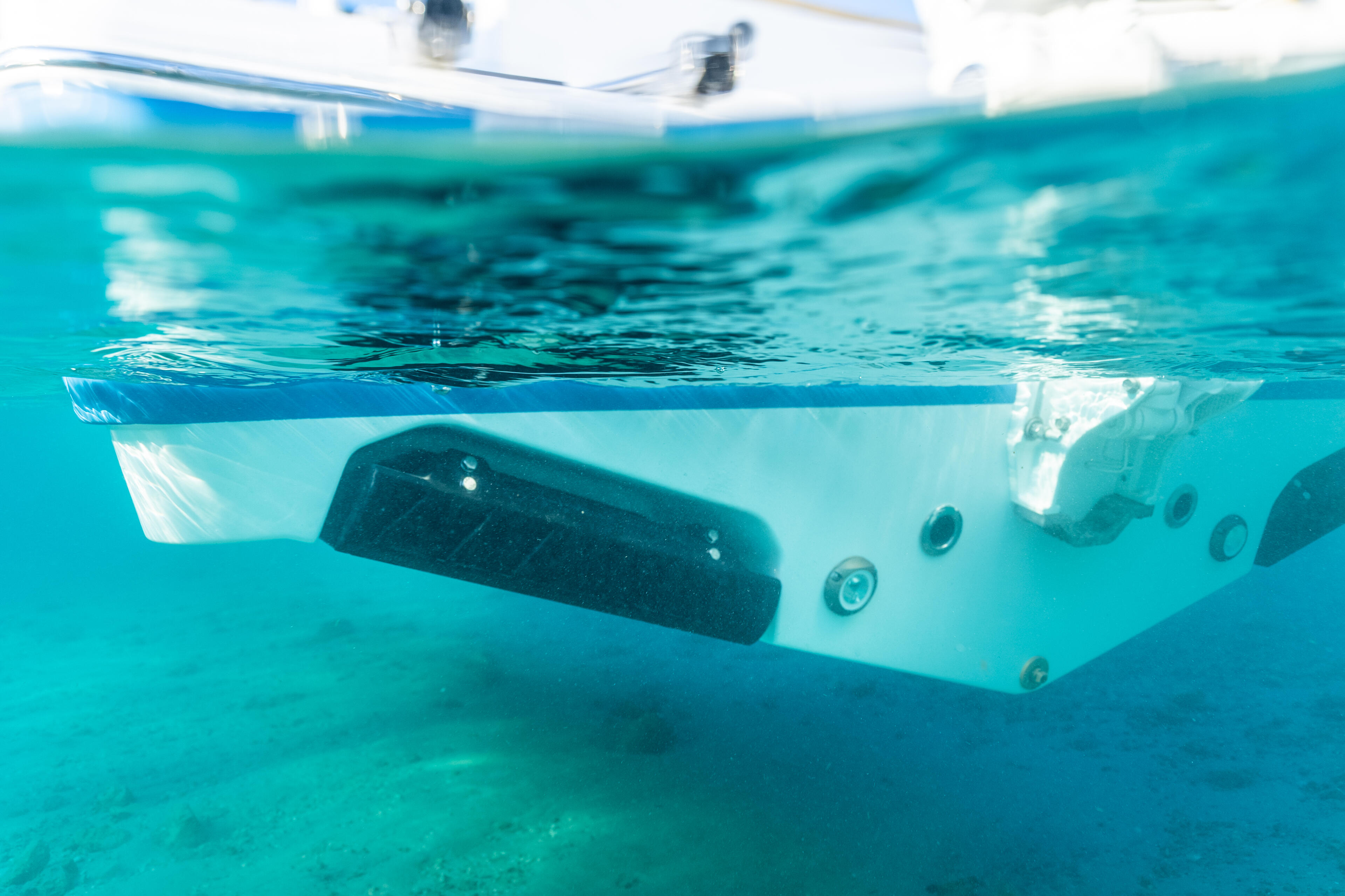 Underwater view of boat hull near sandy bottom in clear turquoise water