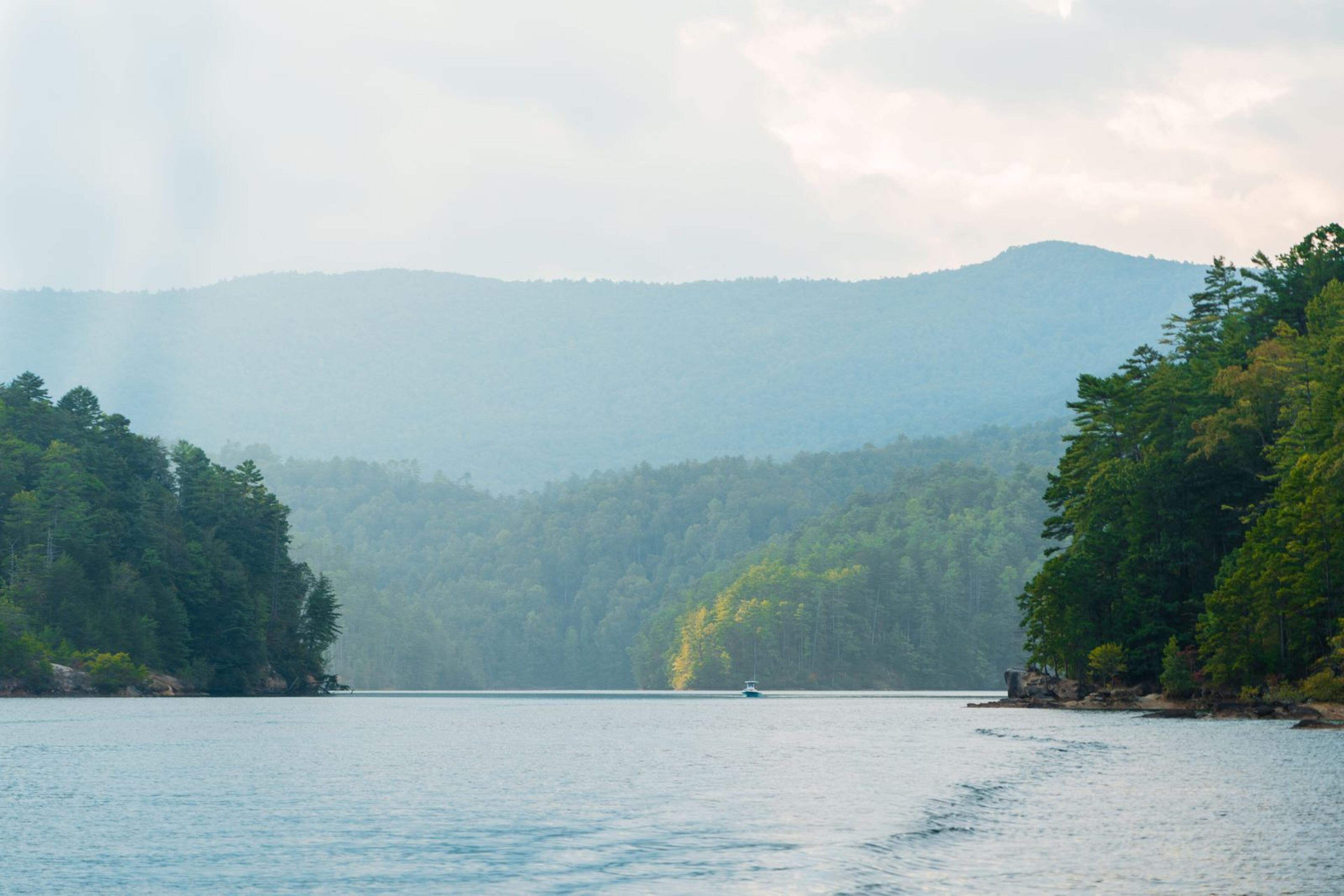 Forested lake surrounded by tree-covered mountains with a small boat in the distance