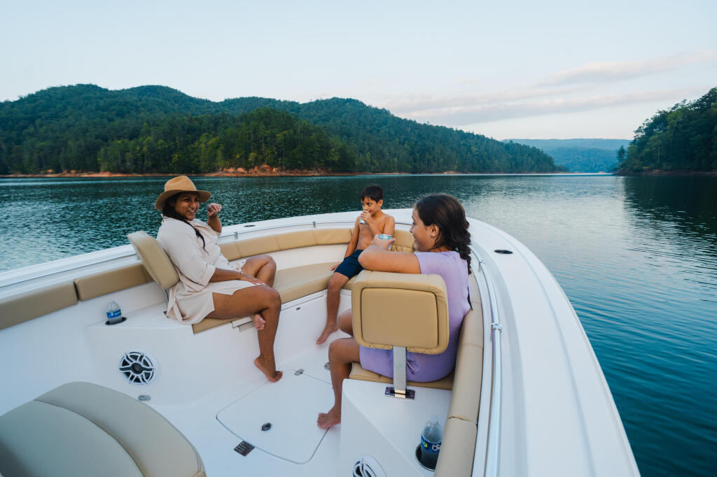 Family relaxing on a boat's spacious seating area with forested mountains and calm lake in the background