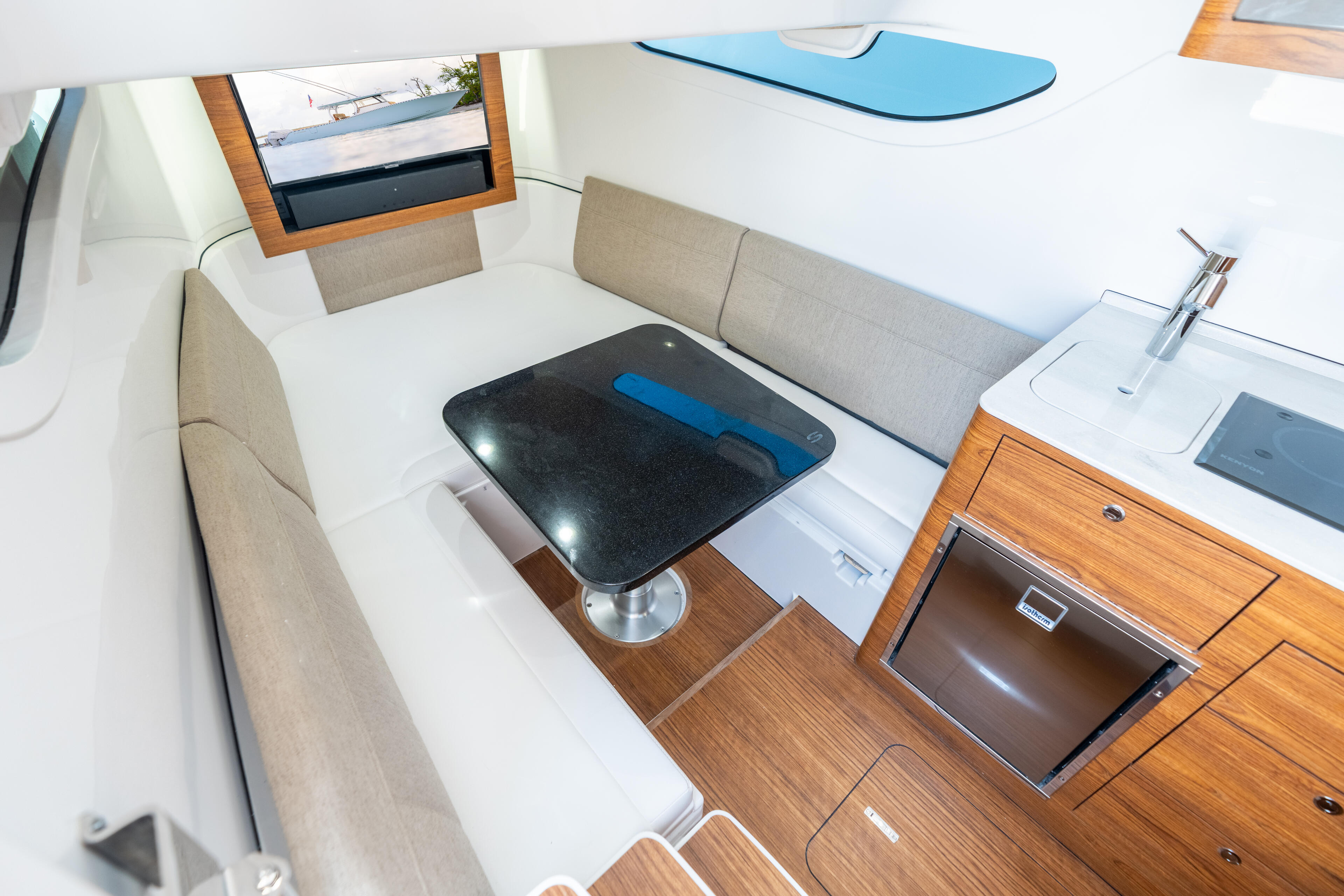 Modern cabin interior with L-shaped beige seating, black table, wood cabinetry, and electronics display overlooking the water
