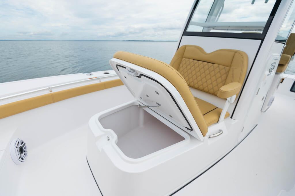 Open storage compartment on boat deck with tan cushioned seating and calm water beyond