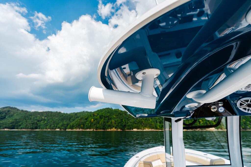 Boat's hard-top with open window frame and white railing overlooking a scenic lake and forested shoreline