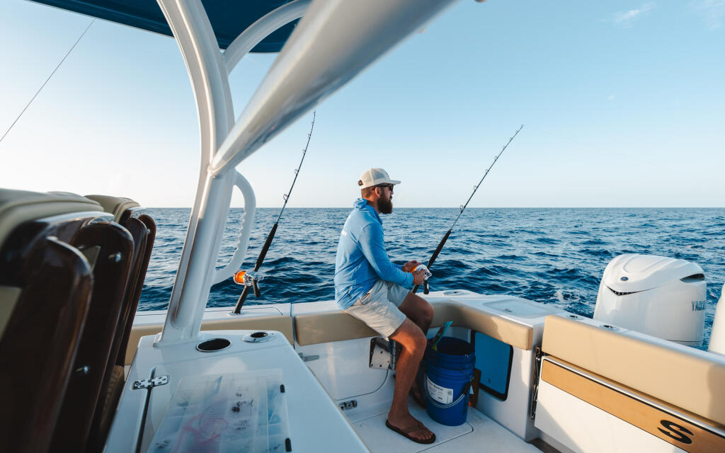 Angler in blue shirt holds fishing rod at helm under hard-top on open water