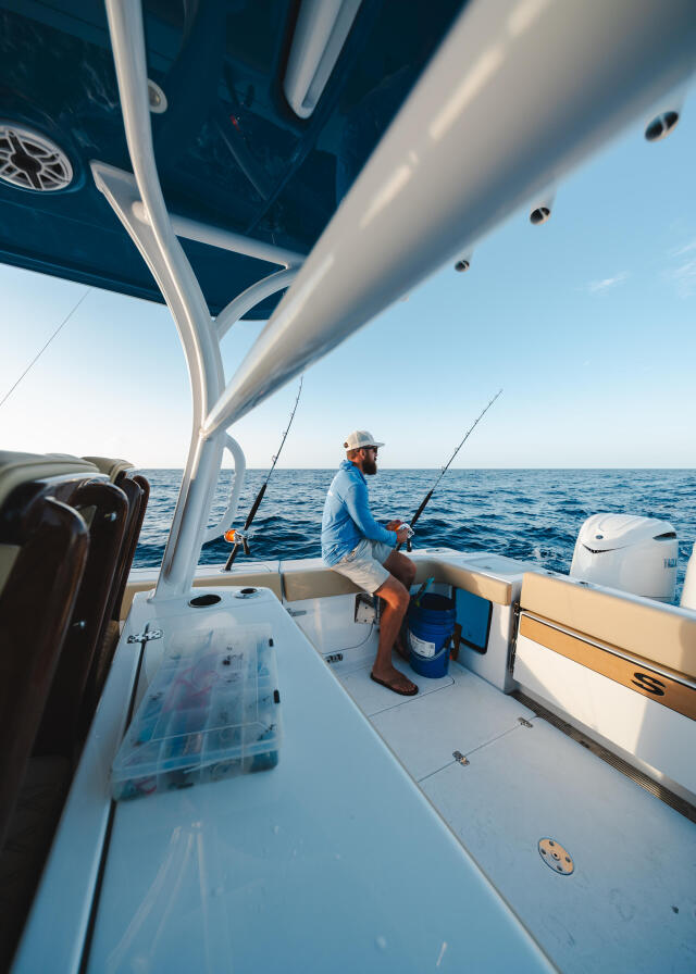 Angler in blue shirt holds fishing rod at helm under hard-top on open water