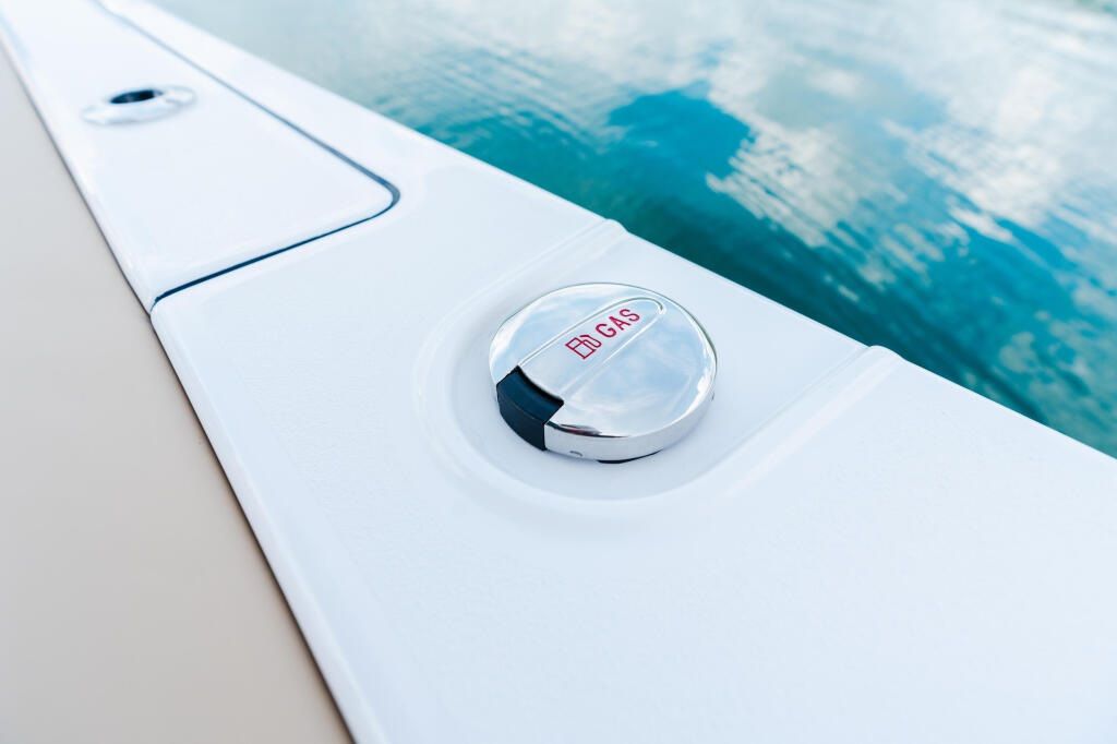 Chrome fuel filler cap on white boat gunwale with turquoise water in background