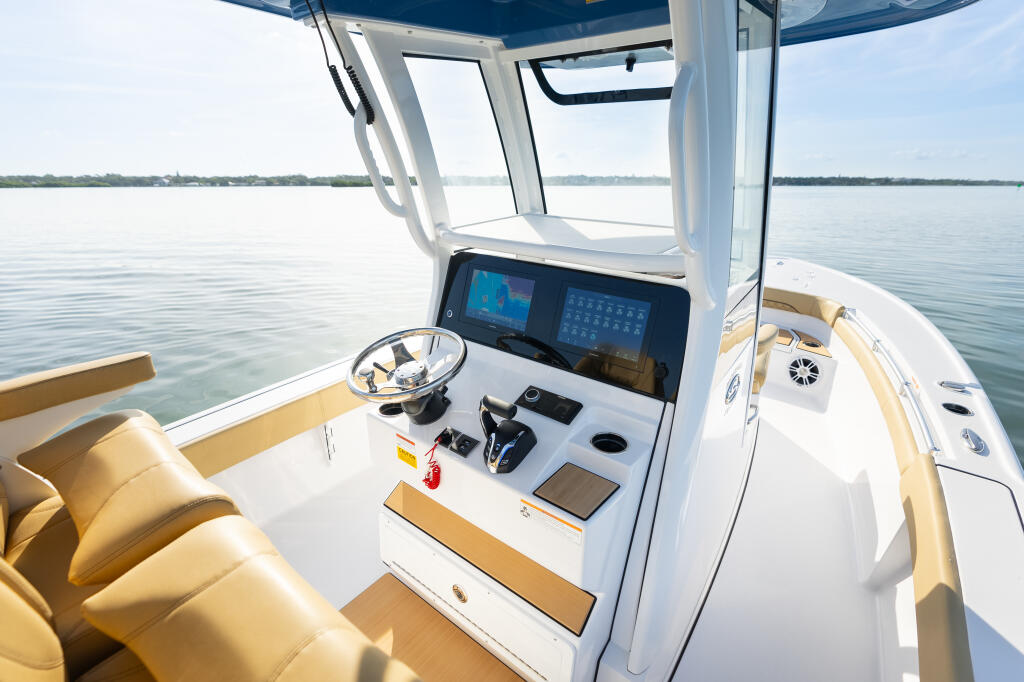 Helm station with dual displays, steering wheel, and tan seating aboard a white center console boat