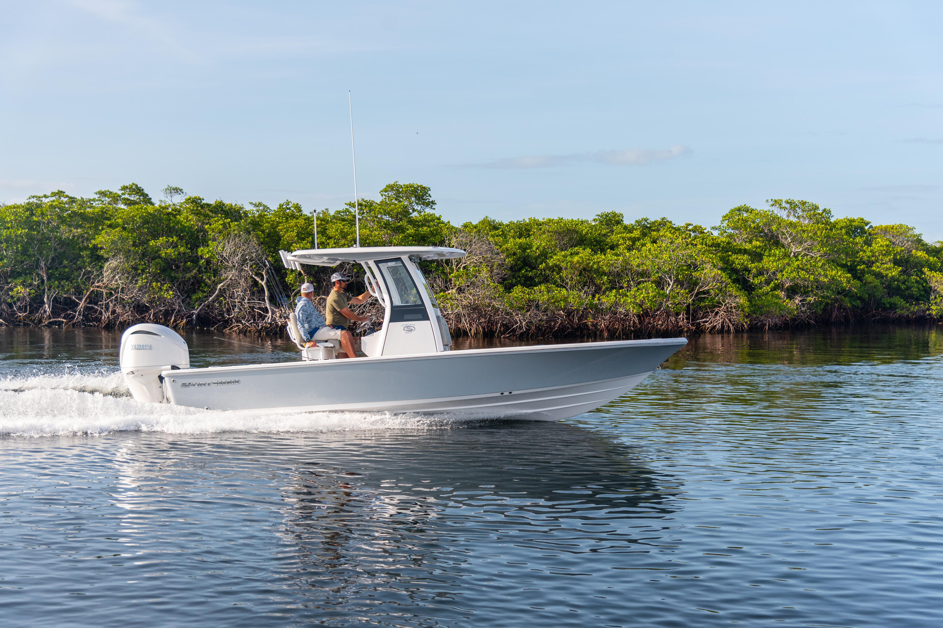 Two anglers navigate a white center console fishing boat through shallow mangrove waters in Key Largo
