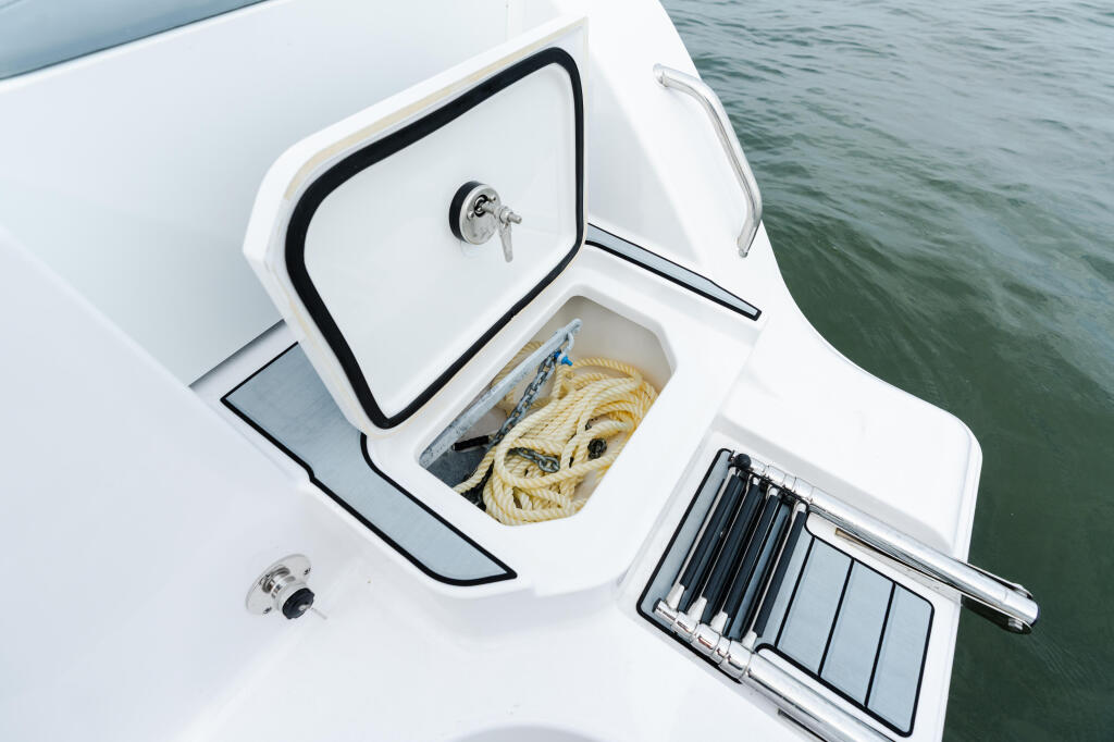 Open storage compartment with rope and fishing rod holder on boat deck near water