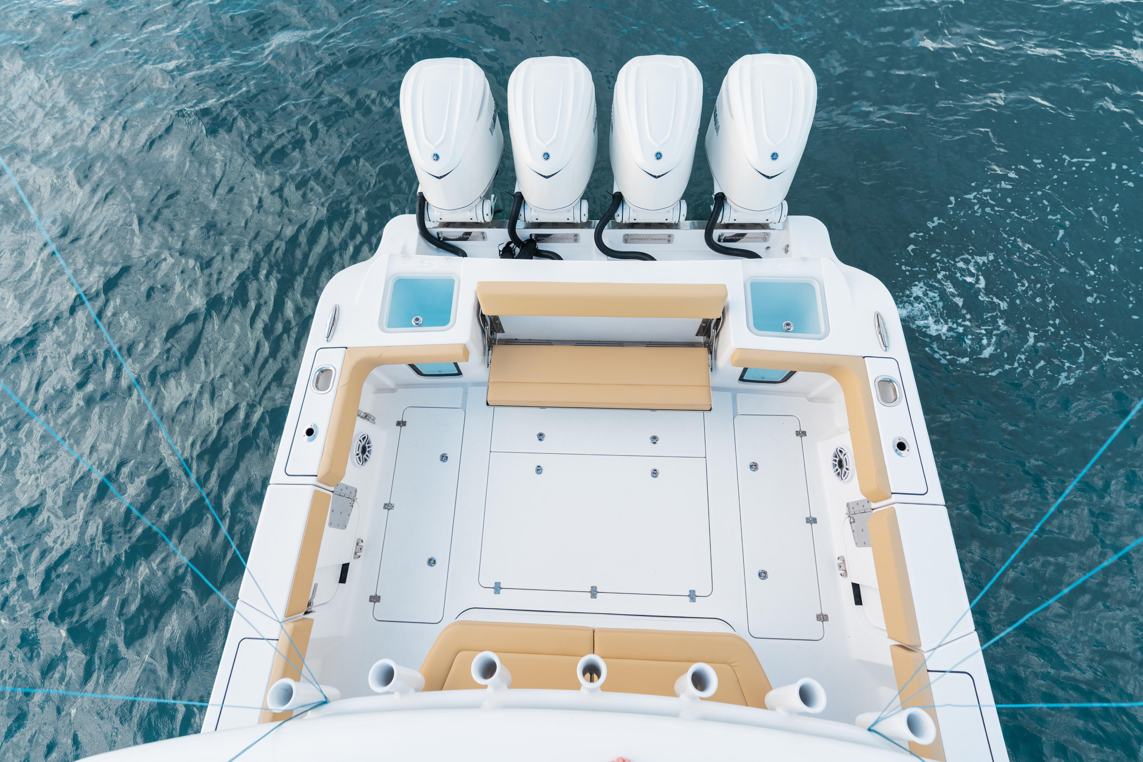 Aerial view of a center console boat's open rear deck with four white outboard engines and tan seating