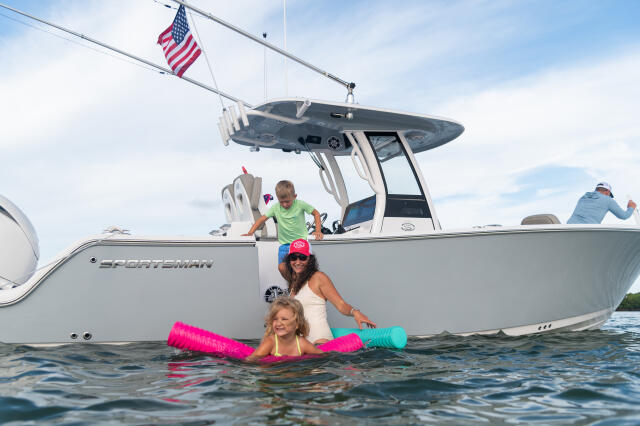 Family swimming and playing in the water beside a Sportsman center console boat with American flag