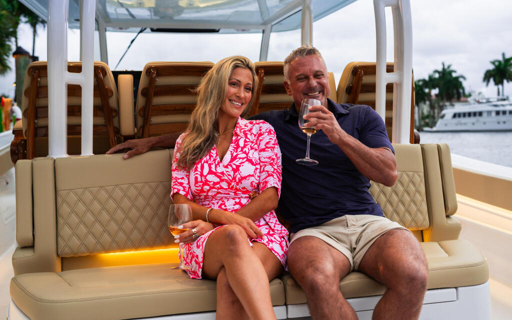 Couple enjoying drinks in the shaded seating area of a boat with marina in background