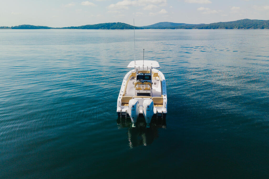 White and blue center console boat anchored in calm clear water with forested mountains in background