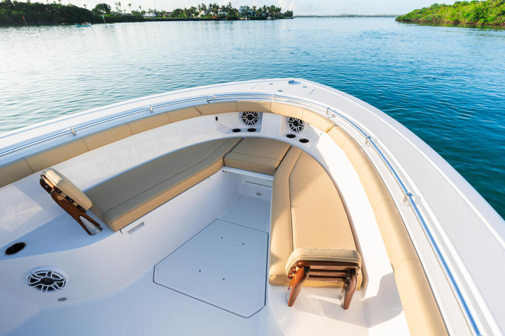 Bow seating area of a white sport boat with tan cushions and speakers, anchored in calm tropical waters with mangrove-lined shores