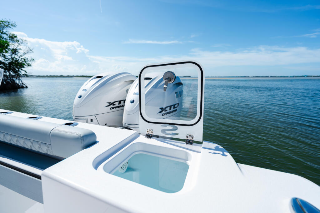 Boat's helm area featuring dual outboard engines, open windshield, and livewell in calm blue water