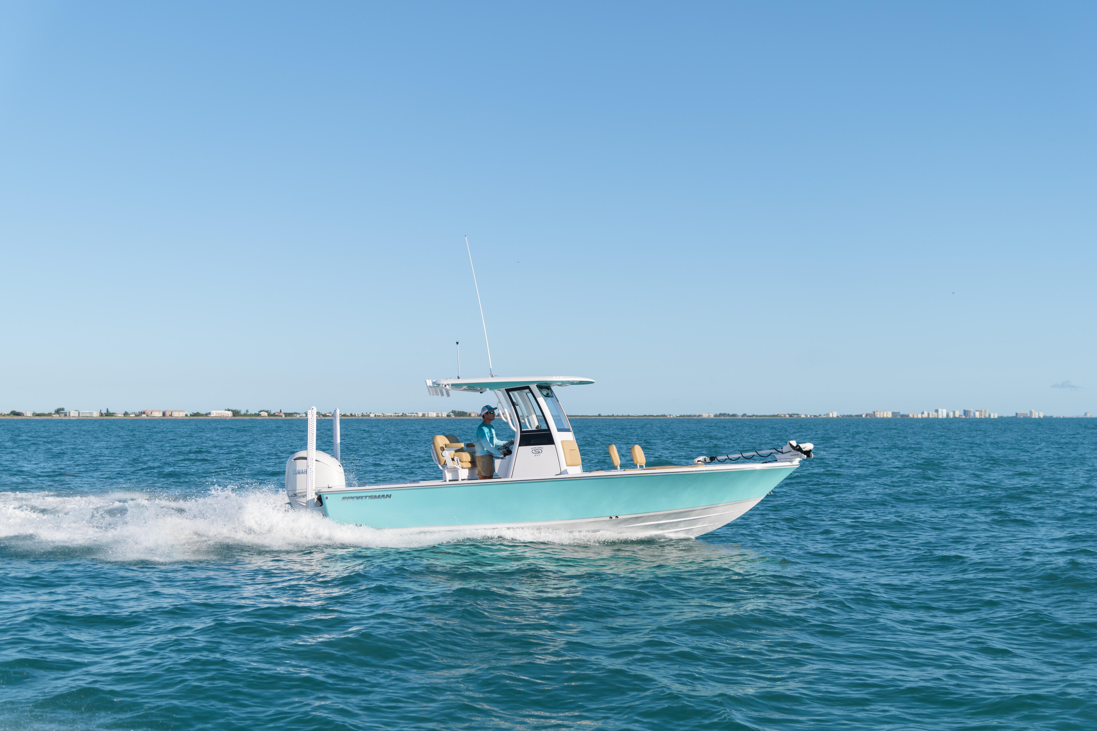 Turquoise center console boat running offshore with two people aboard and coastal cityscape in background