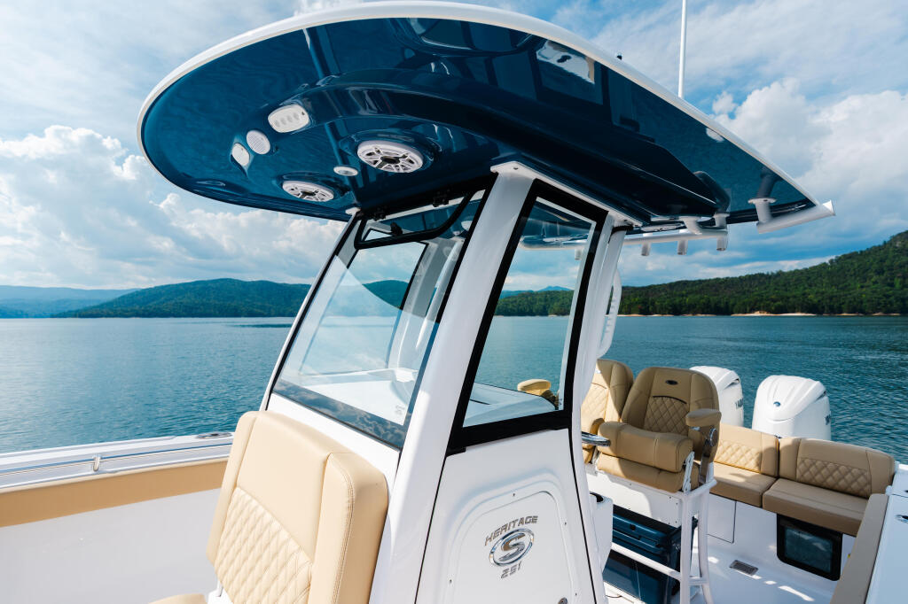 Hard-top boat with cream seating and blue interior helm on calm lake surrounded by forested mountains
