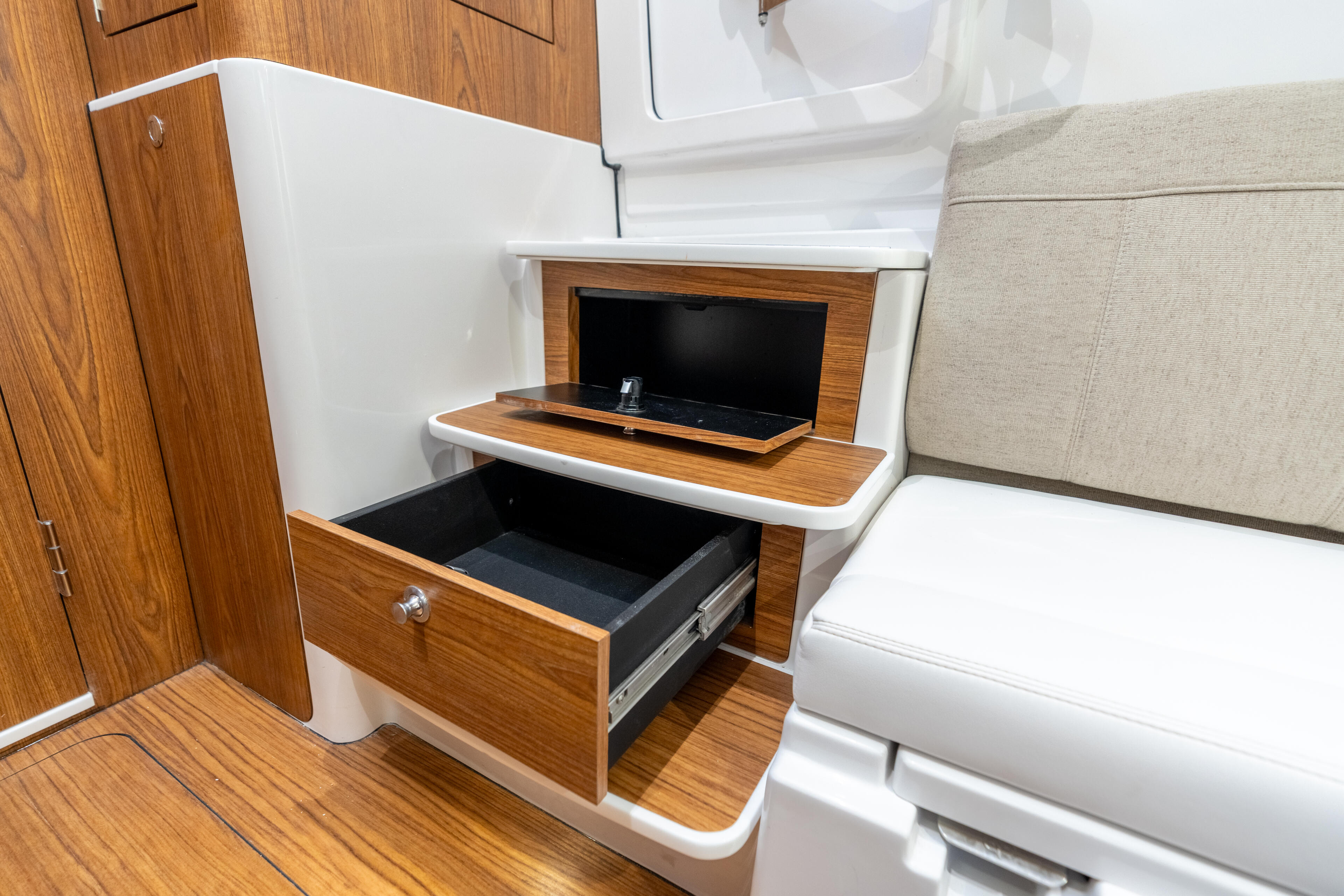 Cabin interior with wood cabinetry featuring open drawer storage and mounted entertainment screen with cushioned seating