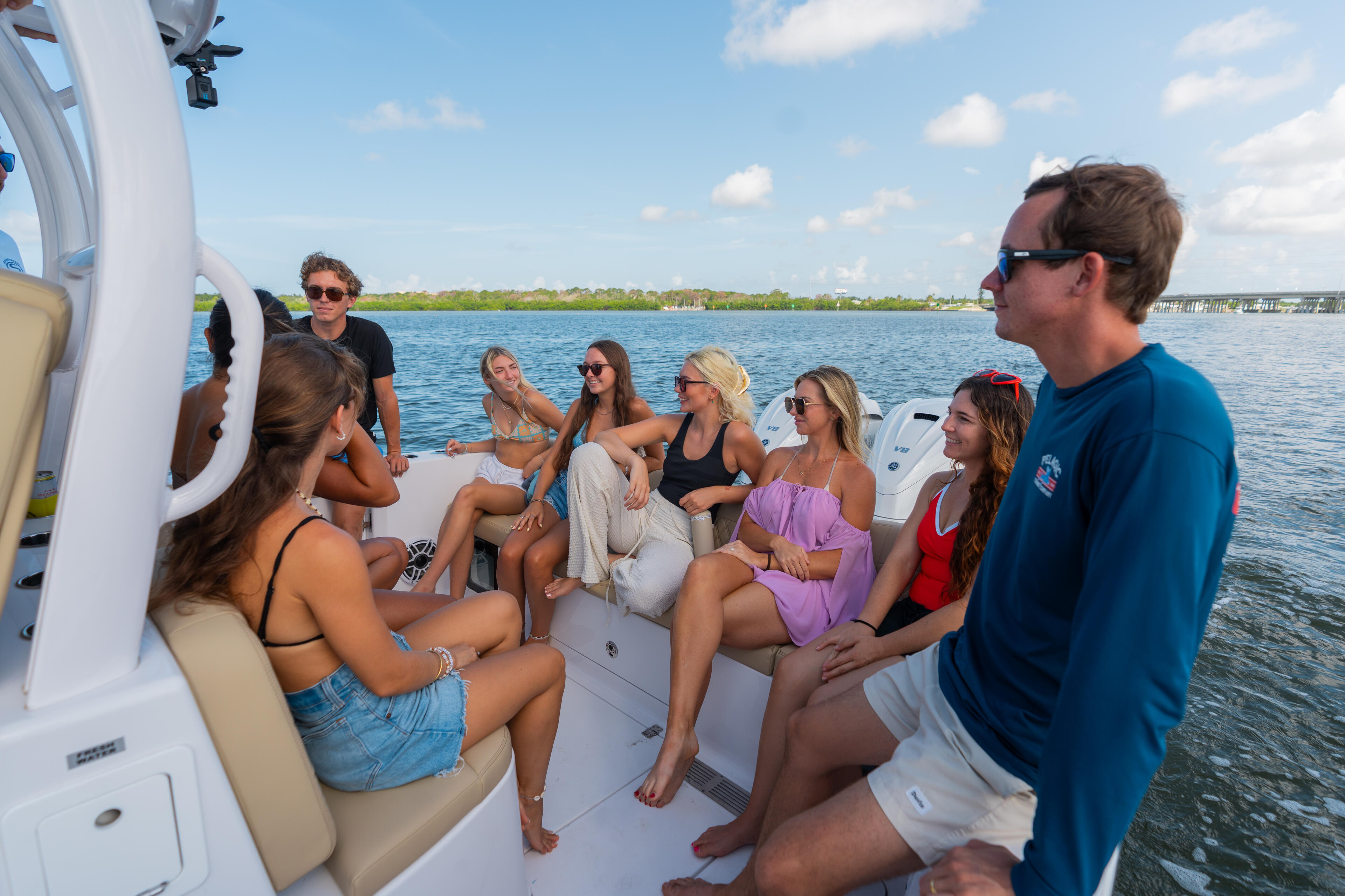 Group of friends gathered in the cockpit of a center console boat, relaxing on a sunny day in calm blue water