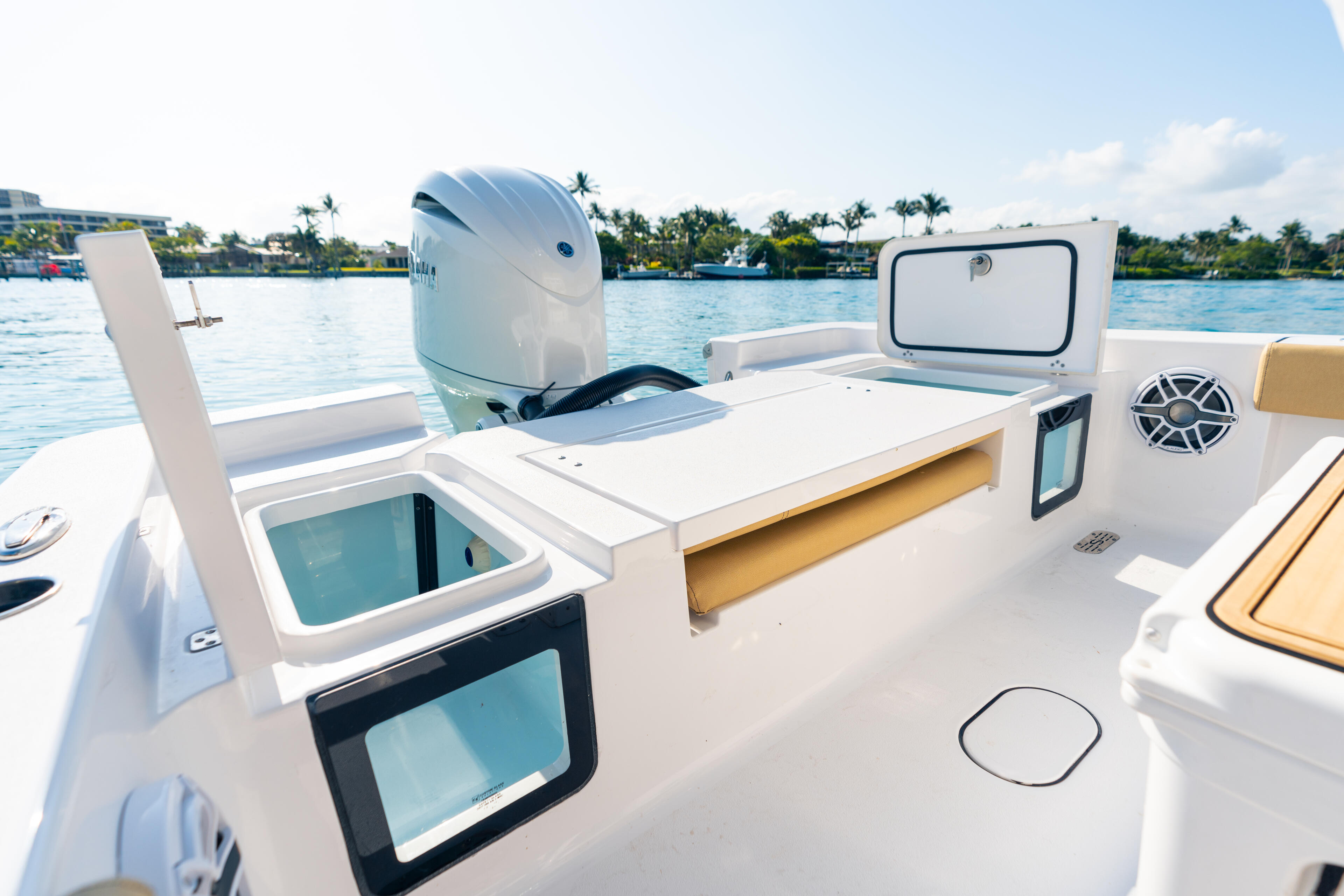 Boat cockpit with livewell, helm station, and outboard engine on calm marina water