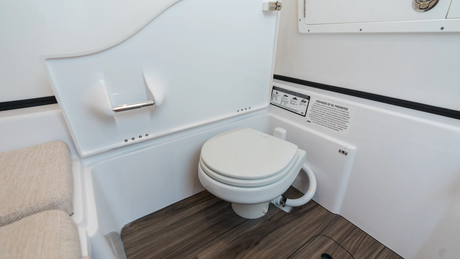 Clean boat cabin head with white toilet, sink, and storage cabinets with dark wood flooring