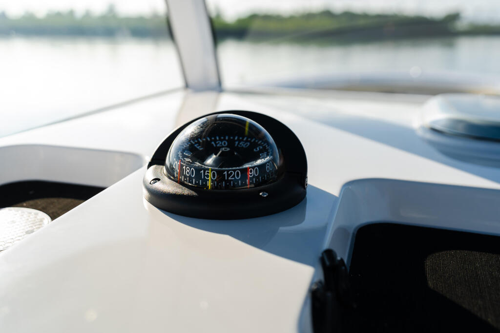 Compass mounted on white boat deck with calm waterway in background