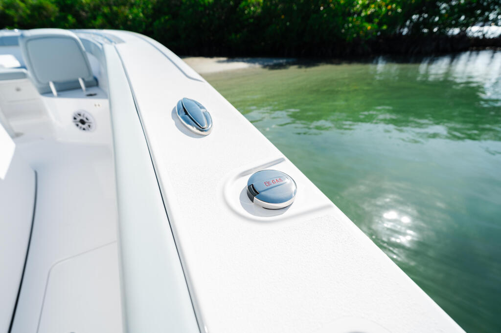 Close-up of white boat gunwale with chrome vents and cleats docked in calm turquoise water