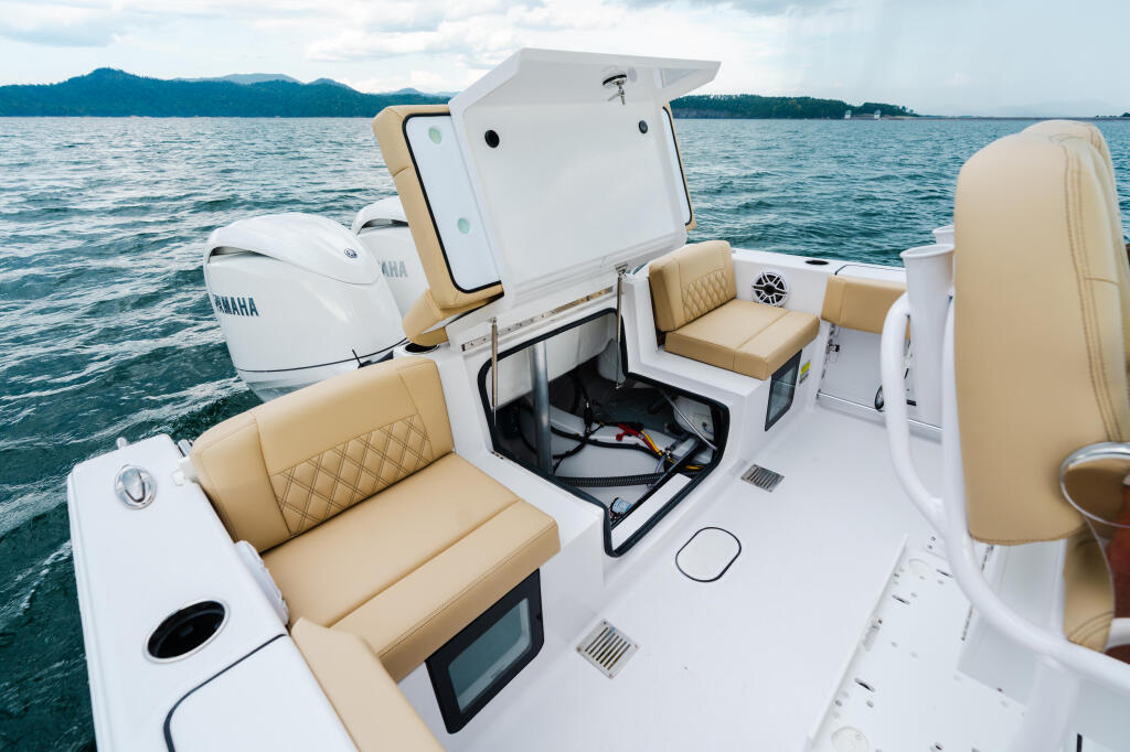 Open cabin console showing tan leather seating, storage compartment, and twin Yamaha engines on a mountain lake