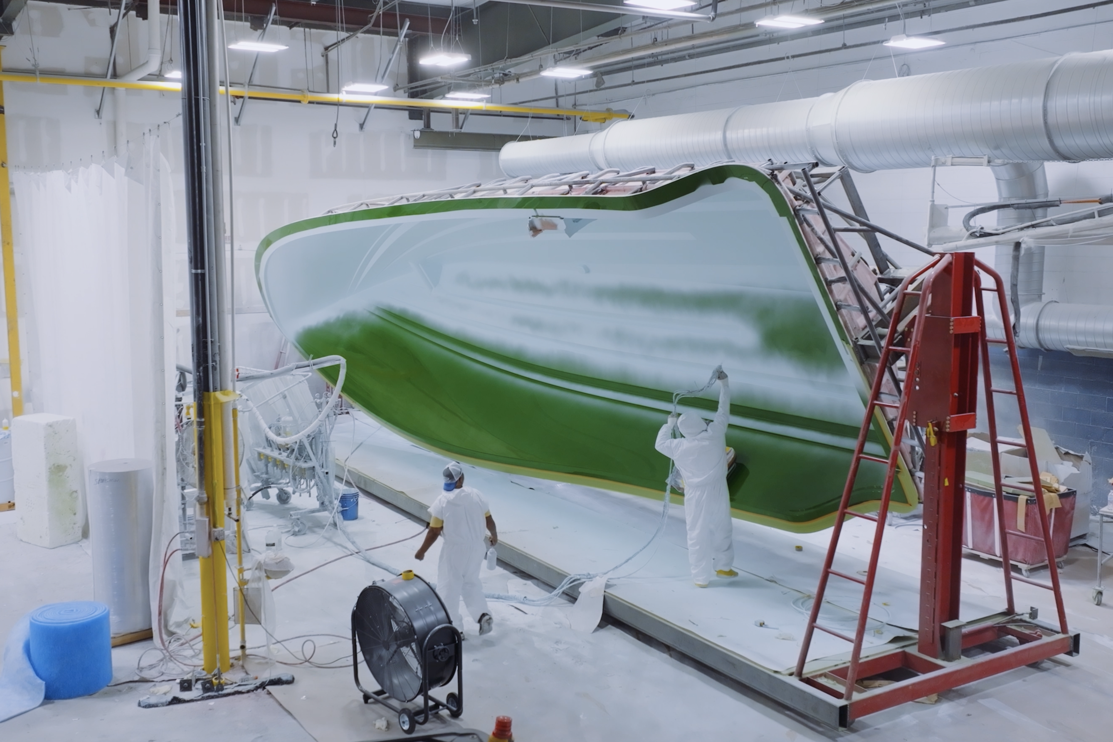 Boat hull under construction in manufacturing facility with workers and industrial equipment