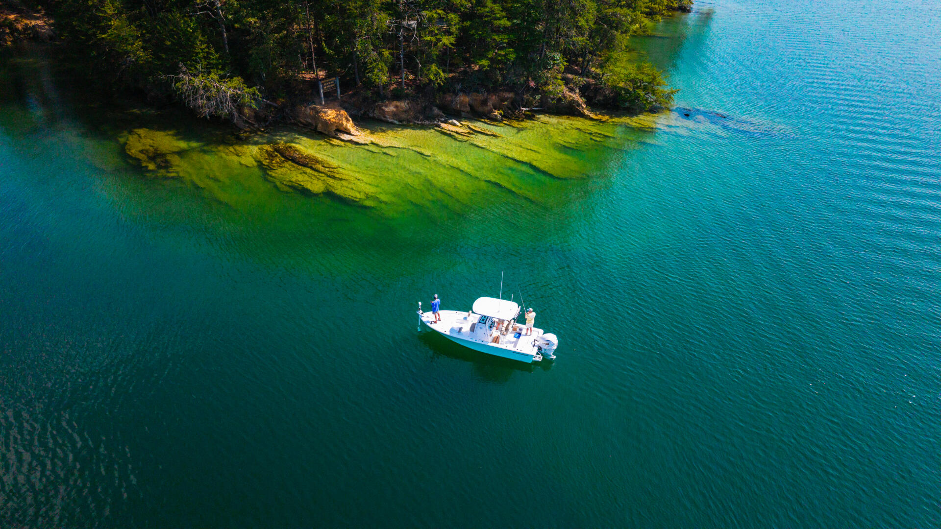 Fishing boat anchored in turquoise water near forested shoreline with rocky outcrops