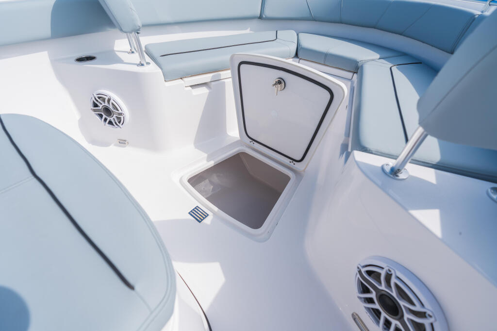 Open in-deck storage box with blue upholstered seating and speaker details on a center console boat