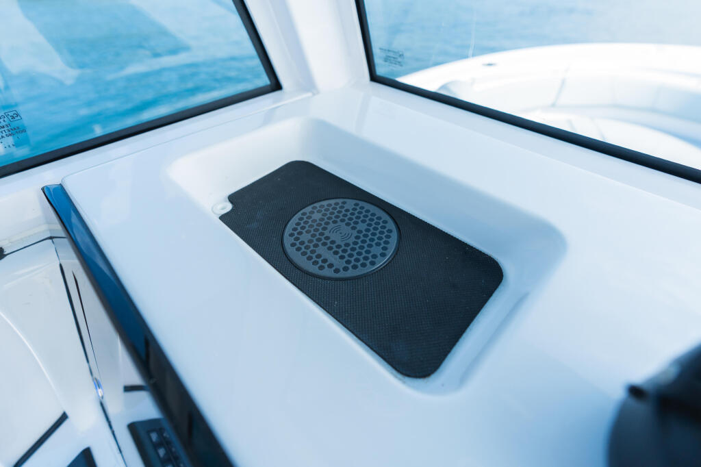 Wireless phone charger pad mounted in white console with blue water and windows visible beyond