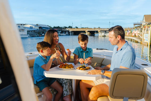 Family of four dining together at a table on a boat docked at a marina