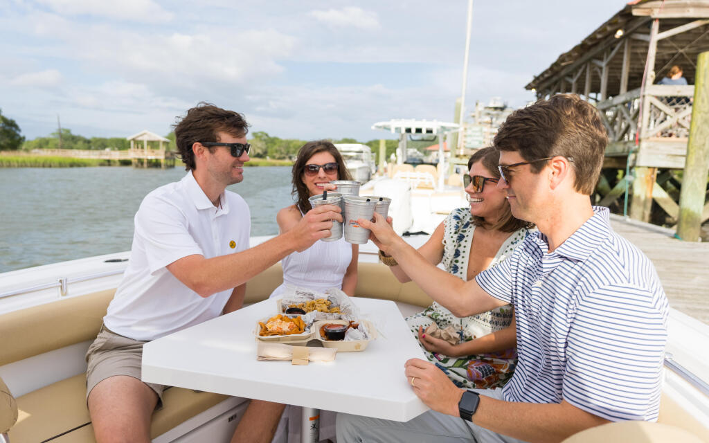 Four friends toasting with drinks while dining on a center console boat docked at a marina