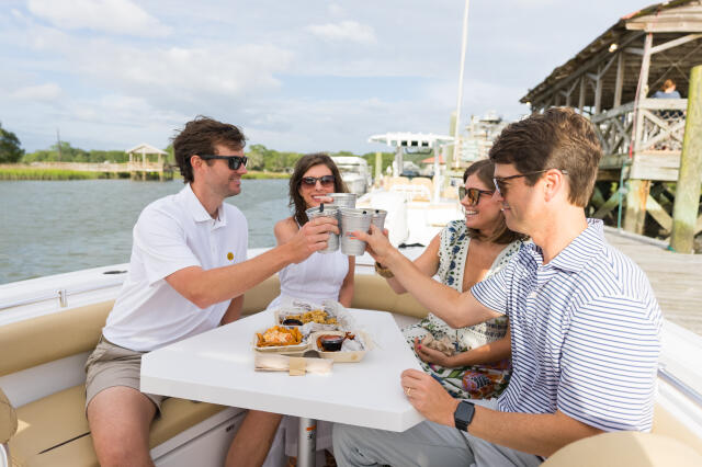 Four friends toasting with drinks while dining on a center console boat docked at a marina