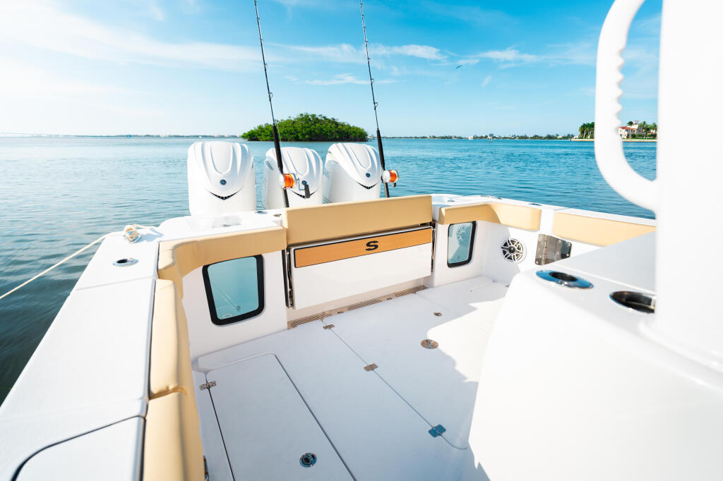 Helm and cabin area of white fishing boat with twin outriggers and tan accents anchored in calm blue water