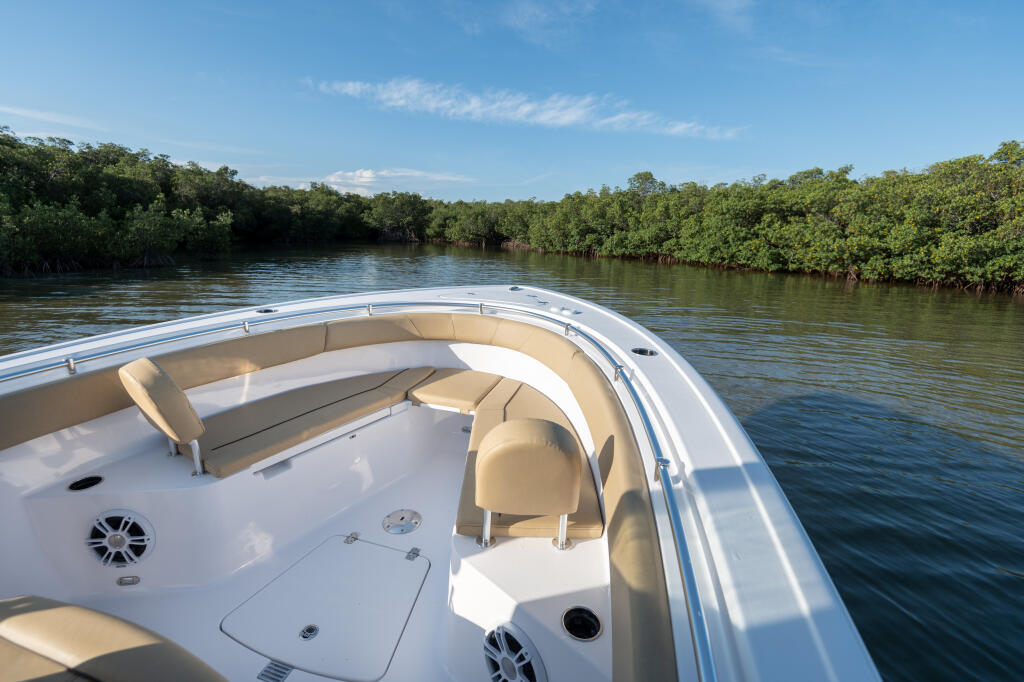 Spacious bow seating area with tan cushions overlooking mangrove-lined waterway