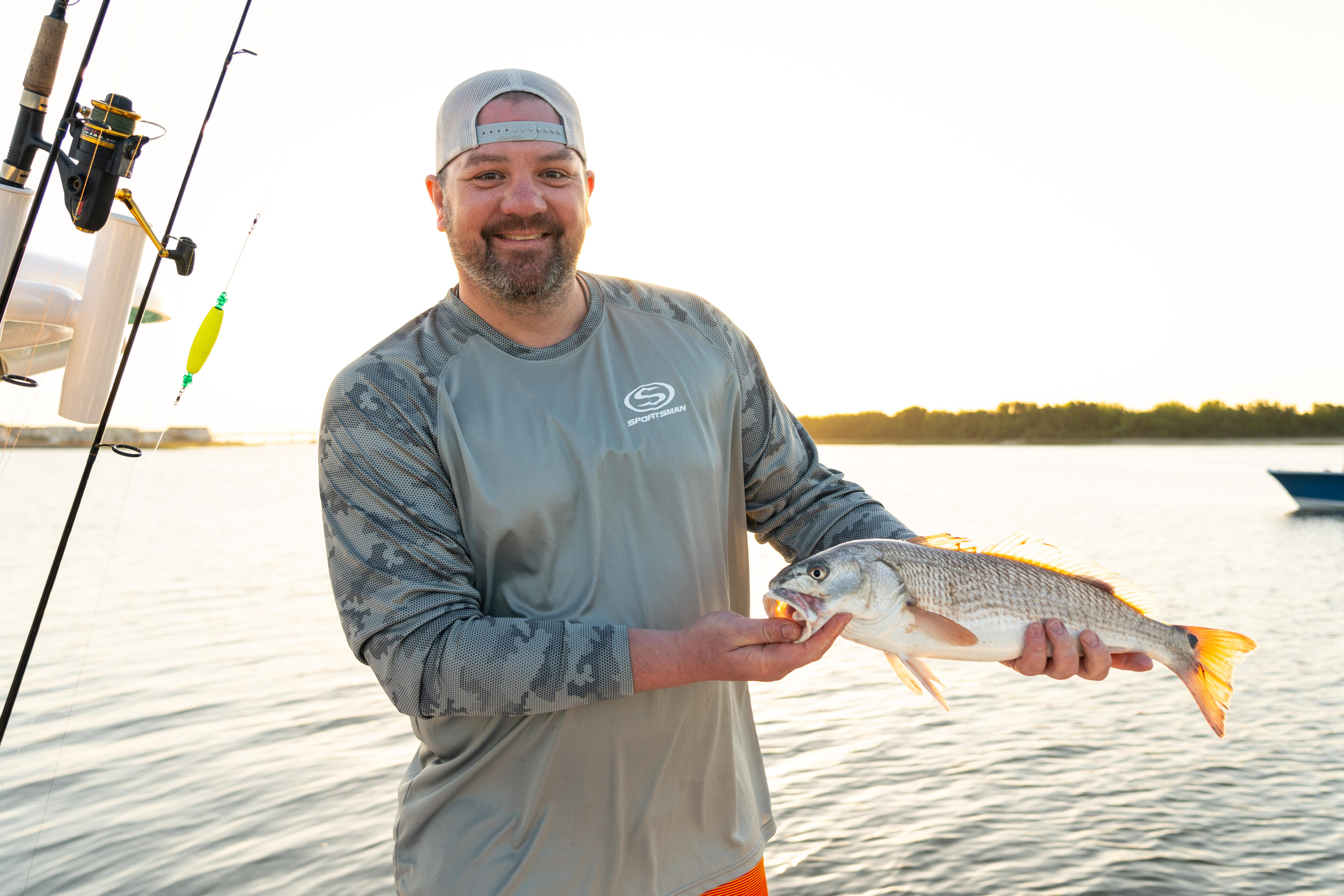 Angler holding a redfish while smiling at the camera on a calm water during golden hour
