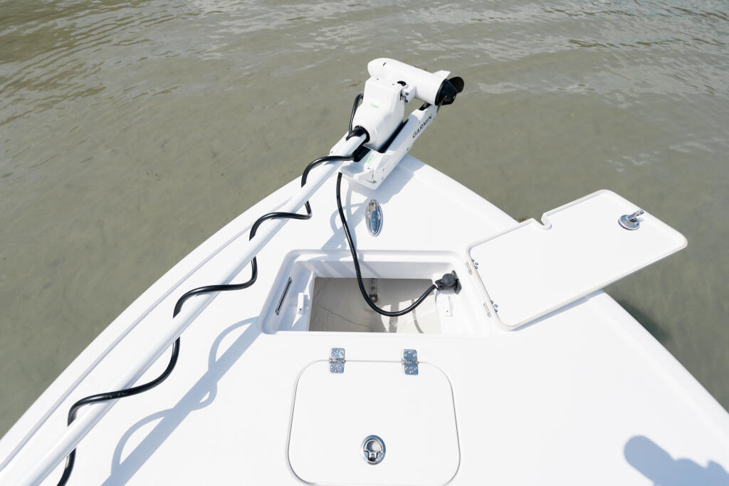 White boat bow with electronic anchor winch and open storage locker on calm water