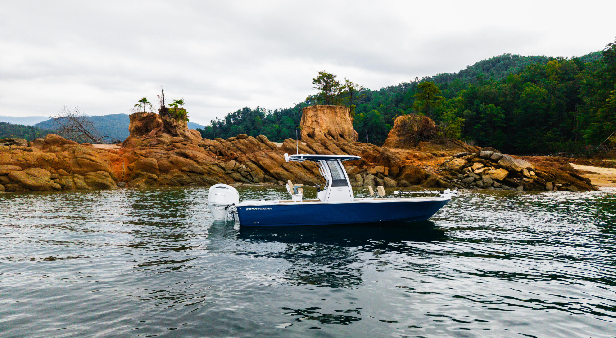 Blue and white center console boat anchored near rocky outcroppings and forested shoreline