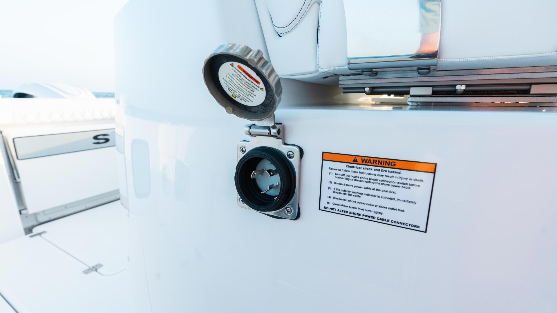 Electrical shore power outlet and warning label mounted on the white exterior of a boat